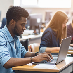 A student tying and looking at an open laptop