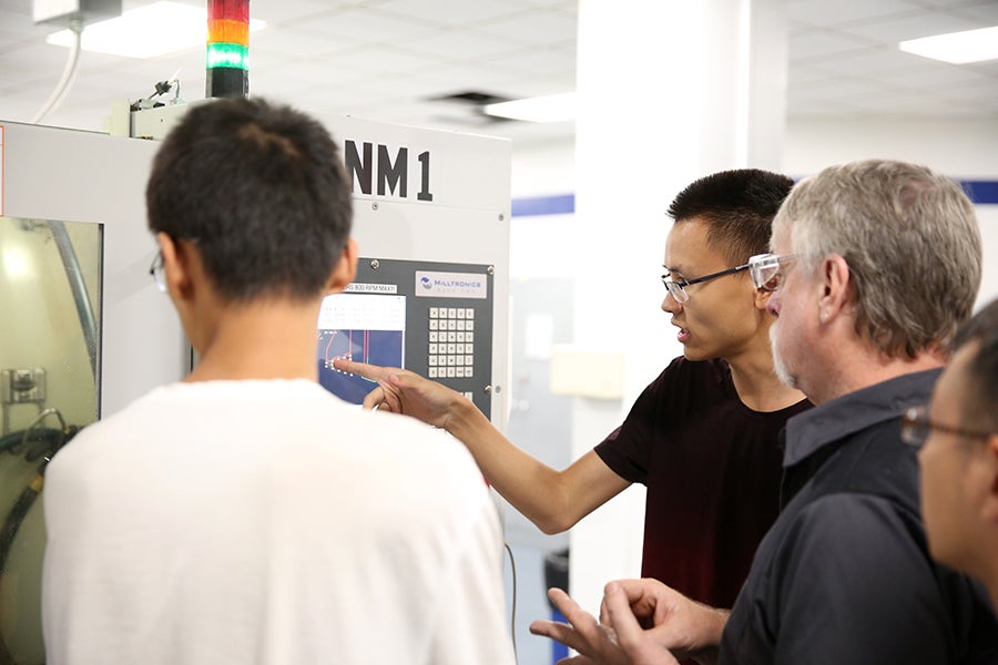 Instructor Paul Craig shows Beijing students how to use a computer numerical control machine in the UW-Stout Fryklund Hall machining lab.