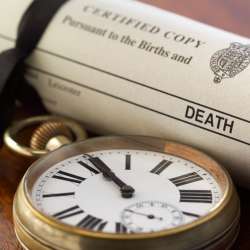 A pocket watch and a certified copy of a death certificate placed side by side on a surface.