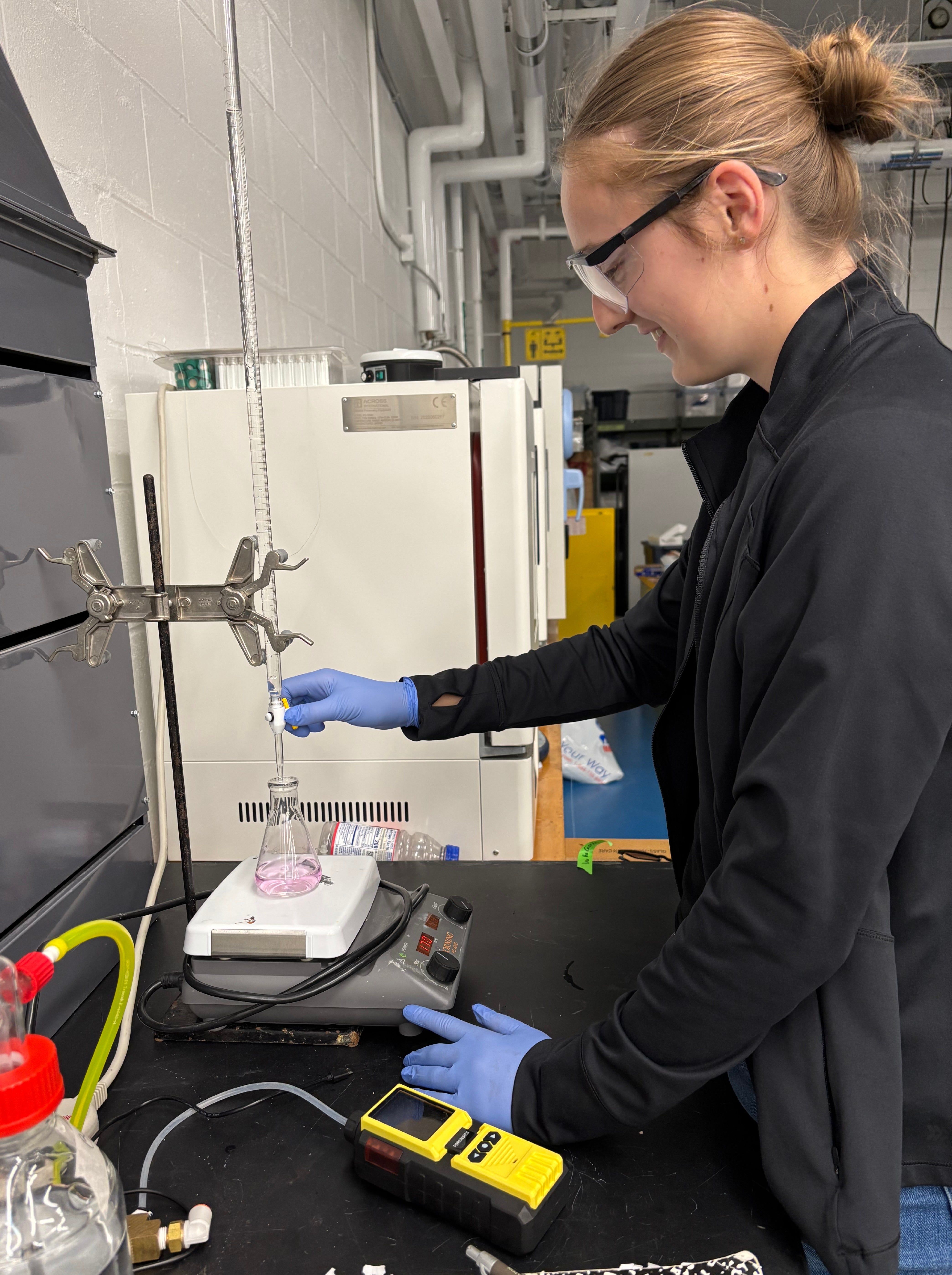UW-Stout student conducts a chemistry experiment, performing a titration using laboratory glassware and safety equipment.