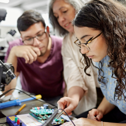 A teacher helping two student pointing at a robotic model