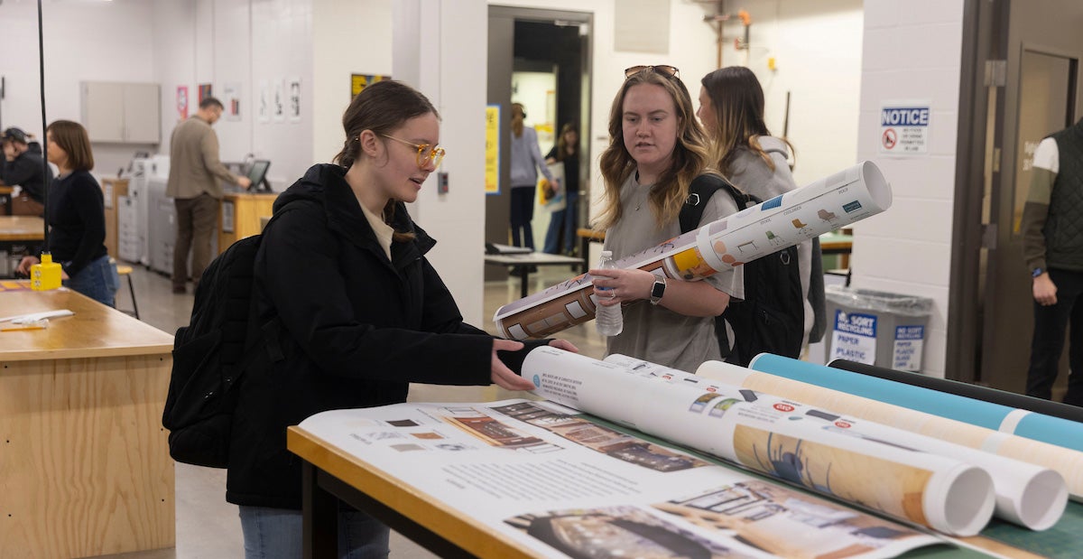 Female students review large format prints for a class project.