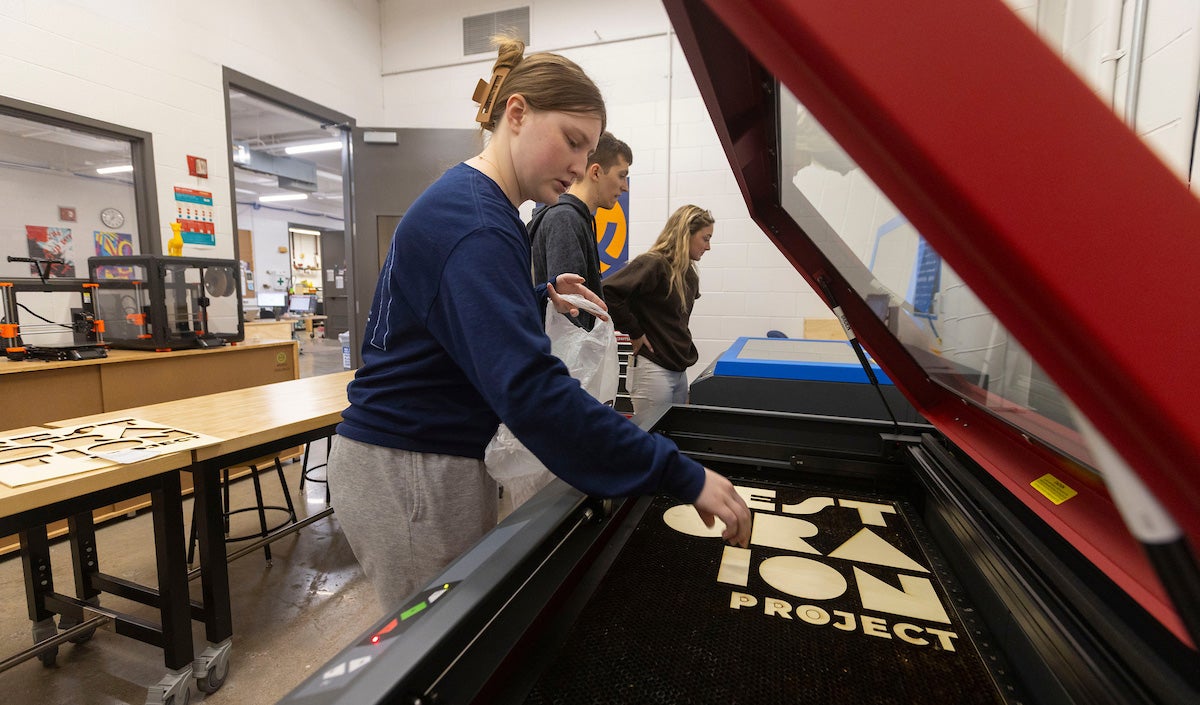A female student removes laser-cut wood letters from a laser cutter.