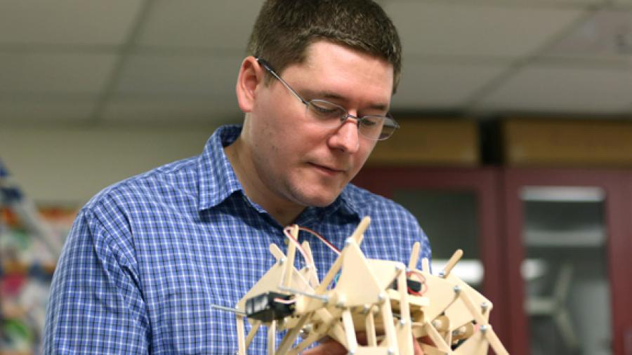 Instructor Kevin Dietsche examines a mechanical-electrical “scrawler,” a 12-legged walking device created by Matthew Harris.