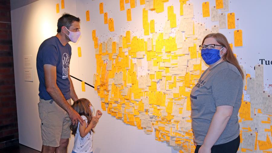 UW-Stout Professor Tom Pearson and his daughter, Zora, with Amy Brostrom, Honors College program assistant, look at some of the toe tags on exhibit at the University Library.