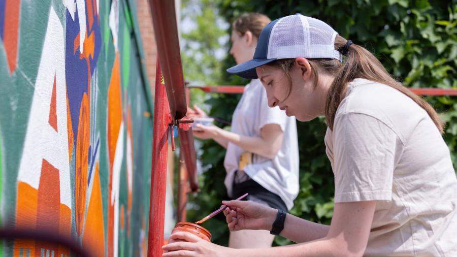 Students paint a colorful mural on a loading dock wall on a sunny day. 
