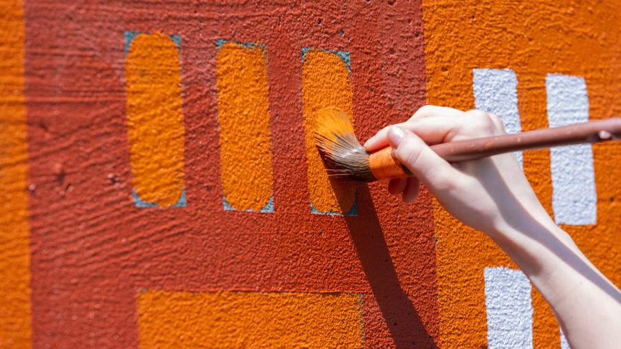 Up close shot of a hand working on some small details, using orange paint.