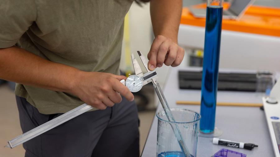 A student measuring the width of a glass cylinder with a caliper