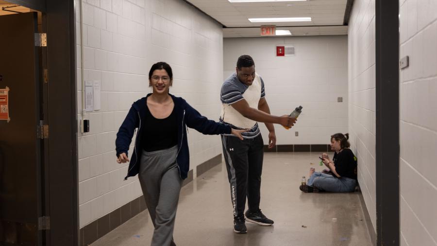 One student shows the other student in their project costume how to walk down the runway