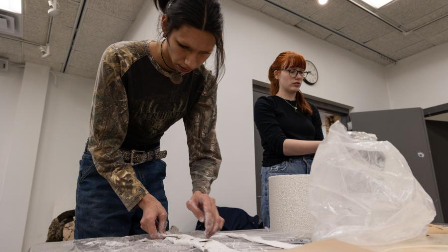 Two students lean over a table working with fabric alternatives to be sewn together for create a unique outfit.