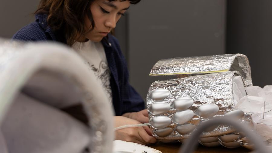 A close up shot of a student and their project, which has silver plastic spoons all over a silver bust.