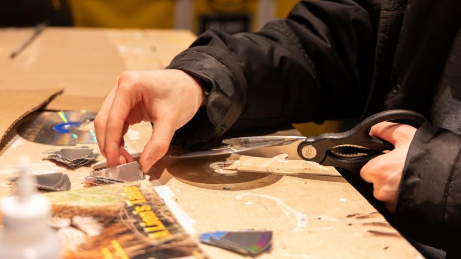 Up close shot of a student's hands holding and cutting up CDs for their Fashion Without Fabric project.
