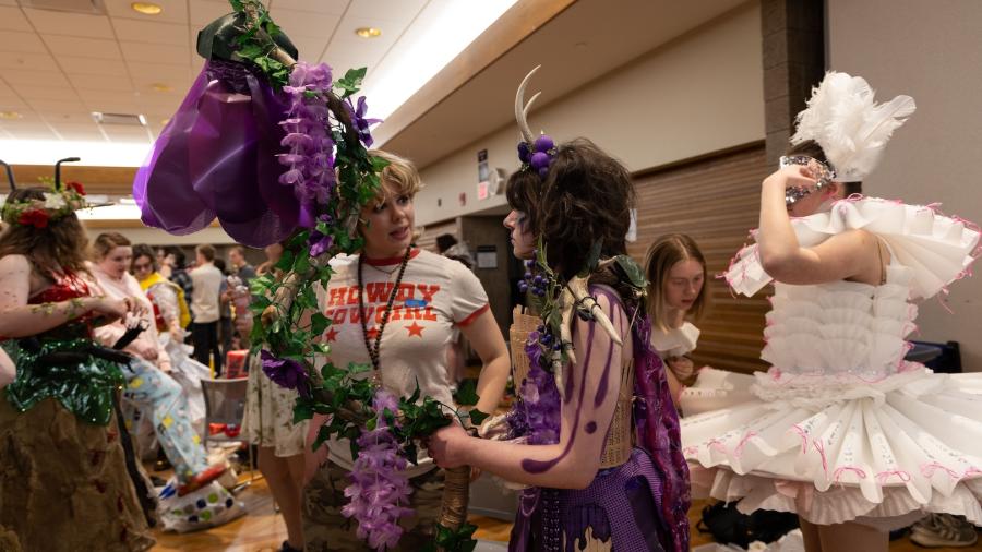 Two students talk as one partner is in their group's wearable project, which incorporates flowers, horns, and fairy-like qualities.