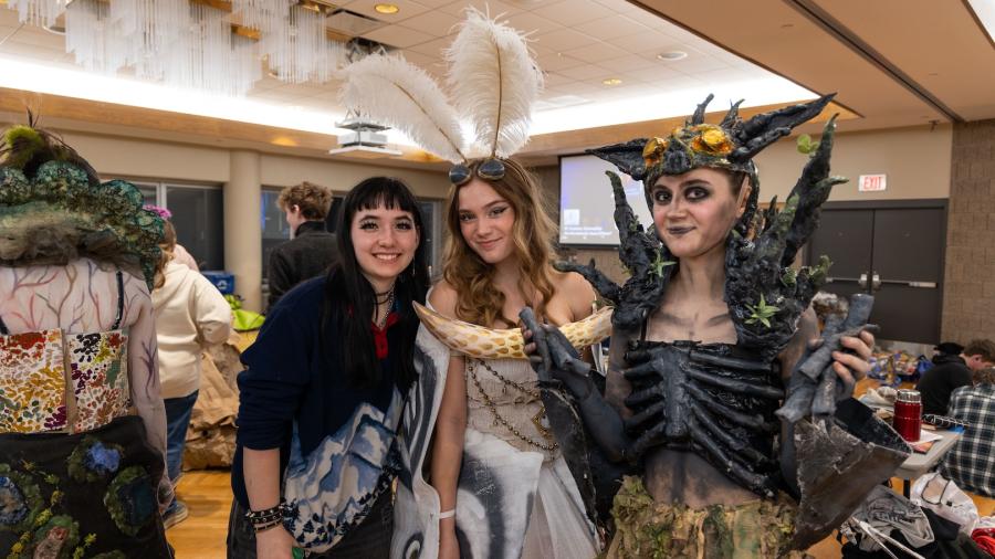 A three-student group stands together and smiles for a picture. Two of them wore fabric-less outfits - one resembling a moth and the other a bat.
