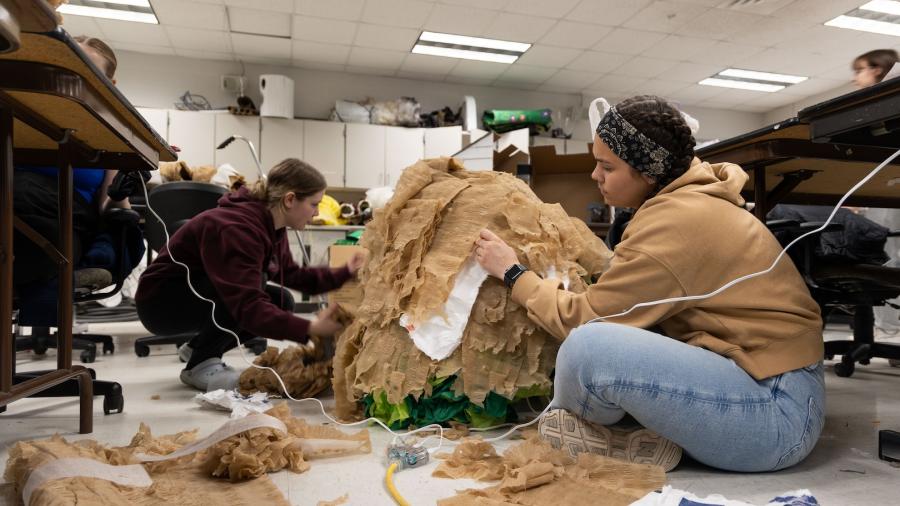 Students sit on the floor as they work on adding details to a large skirt.