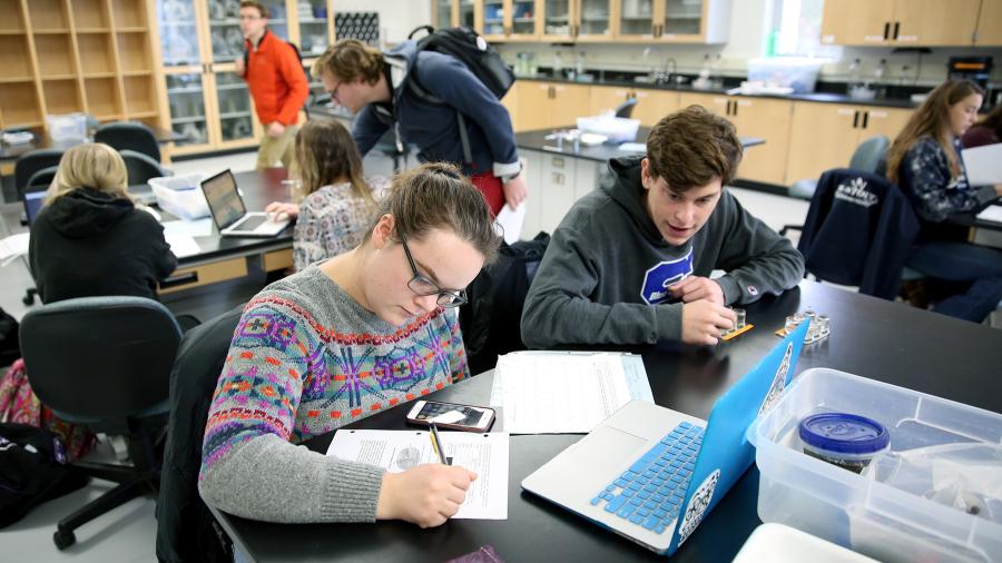 Students working in a biology lab work through quantitative analysis while other student groups work on similar projects in the background.