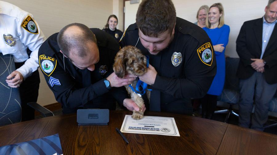 University Police Sgt. Sean Haskamp, left, and Officer Ryan Murray help Officer Harvey put his inked paw on a certificate.
