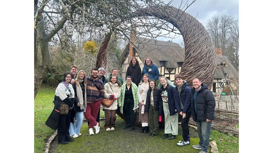 A group of students and professors gather outside of an English Renaissance cottage
