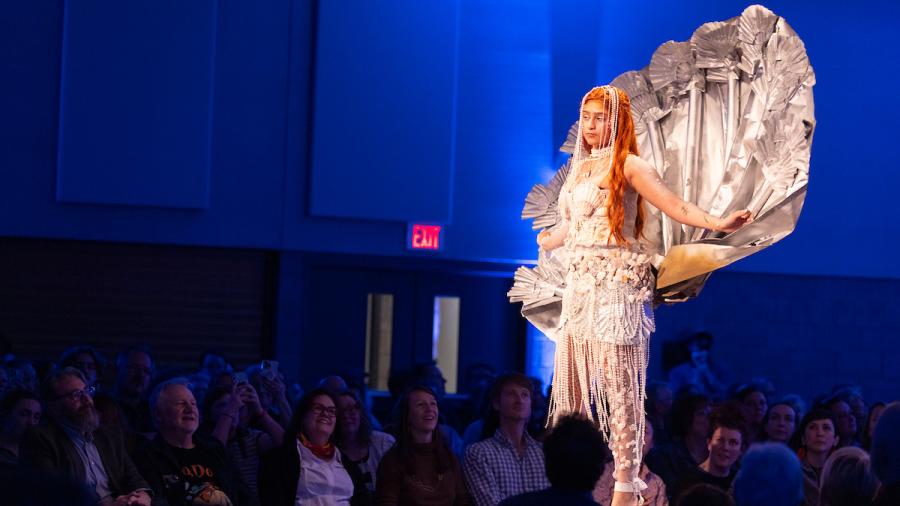 A student models a fashion design with an accent piece that resembles a large pearlescent clam shell