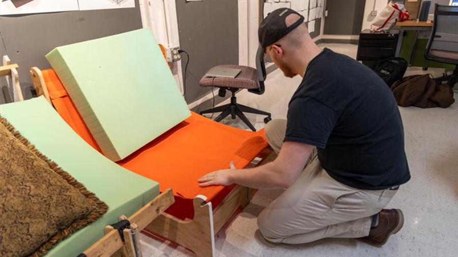 Aaron Hoyt adjusts the upholstery on the wooden frame of his collapsible chair design.