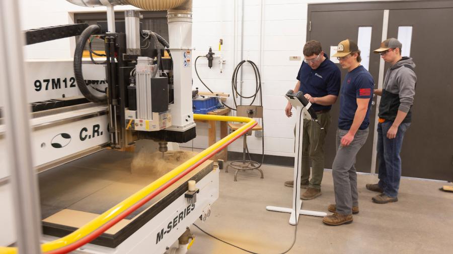 Professor Kevin Dietsche and Braden Kapitz watch as the CNC machine removes wood to shape a main ukulele jig.