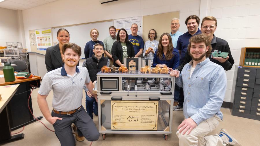 Students, faculty and guests gather around a portable toy assembly machine