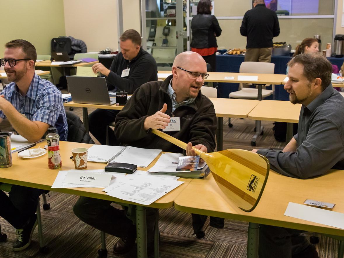 Ed Vater from Branches, LLC, foreground center, discusses business with Jeff Carr, Senior Project Manager from the UW-Stout Manufacturing Outreach Center, as he shows Jeff the BB Special canoe paddle.