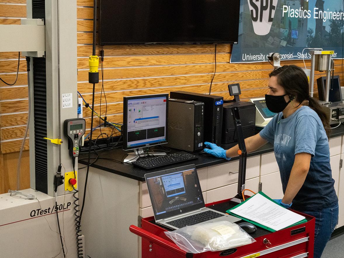 A lab assistant in the UW-Stout Plastics Lab sets up an experiment for students who take readings remotely and use a virtual meetings program to communicate.