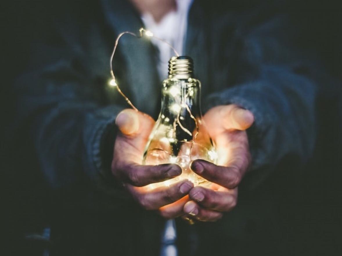 Two hands holding a glowing light bulb.