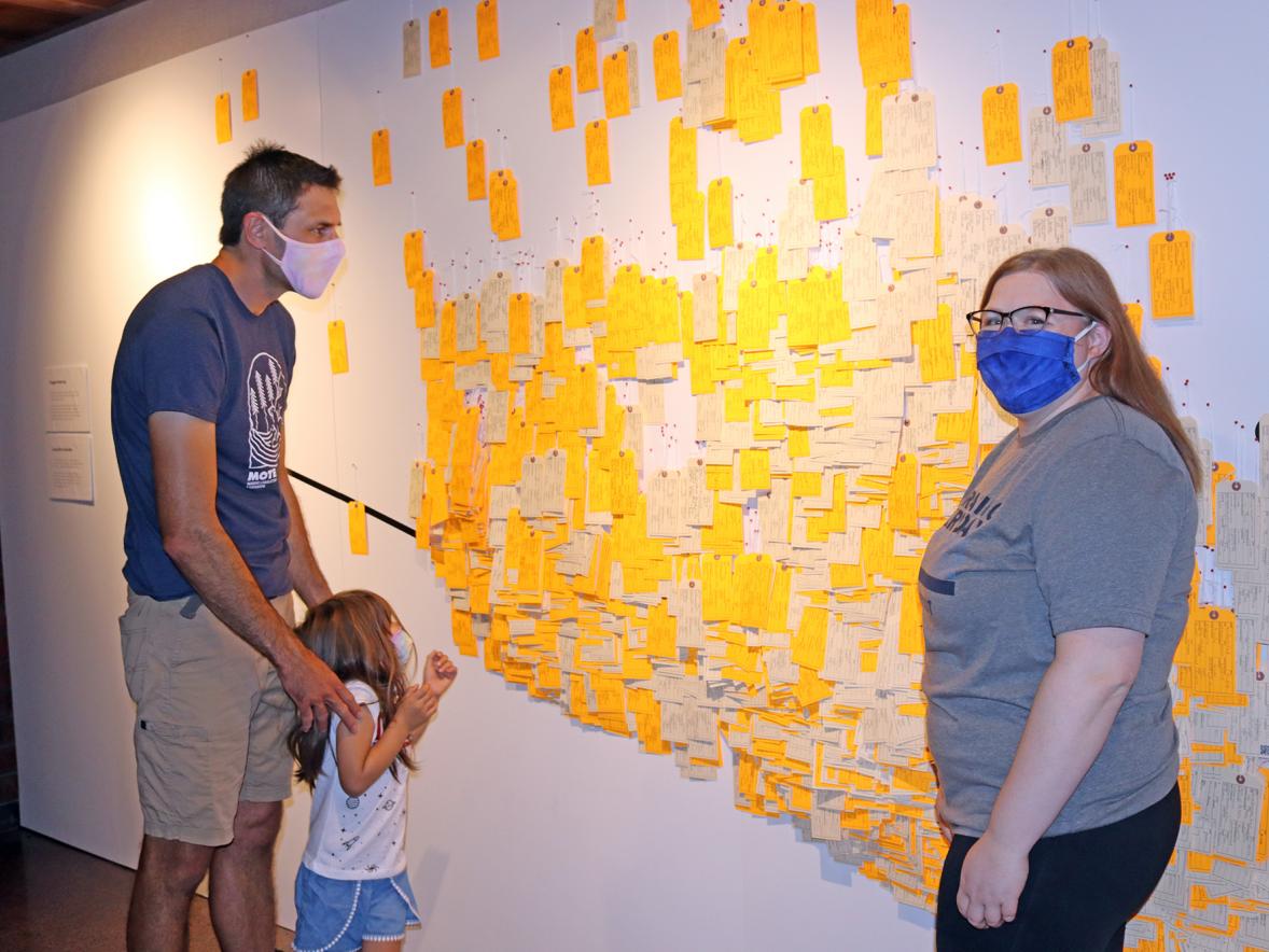 UW-Stout Professor Tom Pearson and his daughter, Zora, with Amy Brostrom, Honors College program assistant, look at some of the toe tags on exhibit at the University Library.