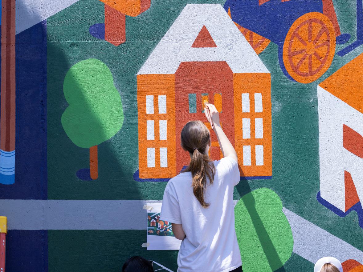 A student paints a large letter 'A' on a mural.