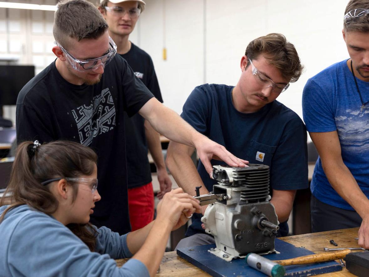 Students hunch over an engine to disassemble it for a class during the first week of the semester.