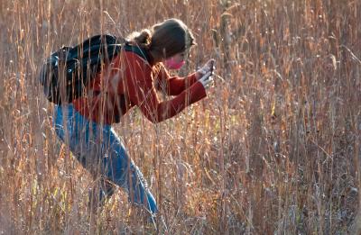 Student Sarah Stein leans down to photograph some plants at Menomin Park.
