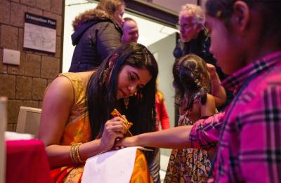A student decorates a child's hand with henna.