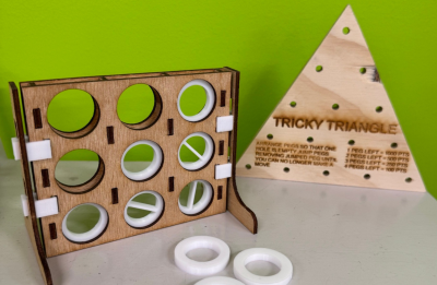 Two wood game placed on a tabletop. One of the game is the Connect 3 and the other piece is the Tricky Triangle puzzle. 