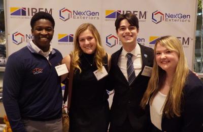 Four people stand shoulder to shoulder in business attire in front of a step-and-repeat backdrop displaying IREM and NexGen Exteriors logos.