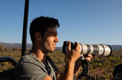 Noah uses a camera with a telephoto lens while riding in an open vehicle in a desert landscape.