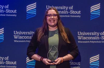 Megan stands in front of a UW-Stout backdrop holding the 2026 Co-op Education & Internship Student of the Year award.