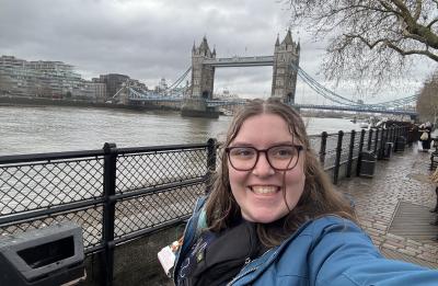 Megan Schatz poses along the River Thames in London with Tower Bridge visible in the background during a faculty-led study abroad experience in England.