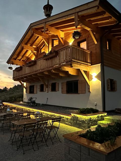 An illuminated chalet at dusk with outdoor seating on a gravel patio and mountains silhouetted in the background.