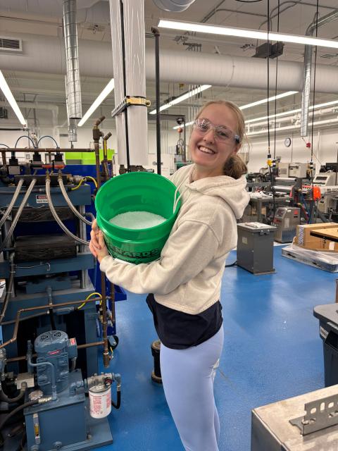 UW-Stout student works in a plastics lab holding a prepared polymer blend sample near laboratory equipment.