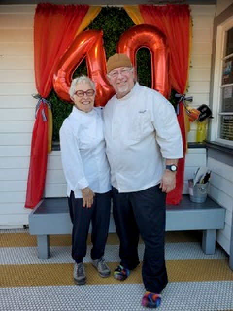 Two people standing in front of large gold number balloons and colorful drapery decorations.