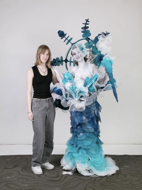 Julia stands beside a model wearing an elaborate blue-and-white costume featuring layered textures and sculptural elements.