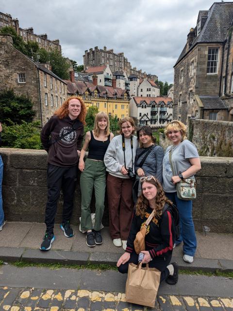 Julia poses with fellow students on a historic stone bridge with traditional buildings rising behind them.