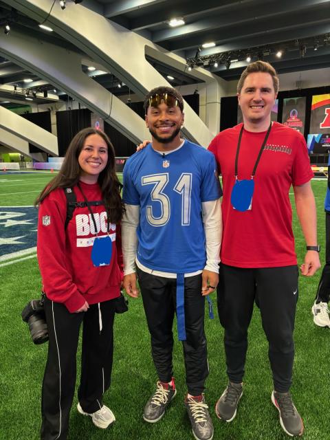 Three people stand together on an indoor football field during a Pro Bowl event, posing for a photo.